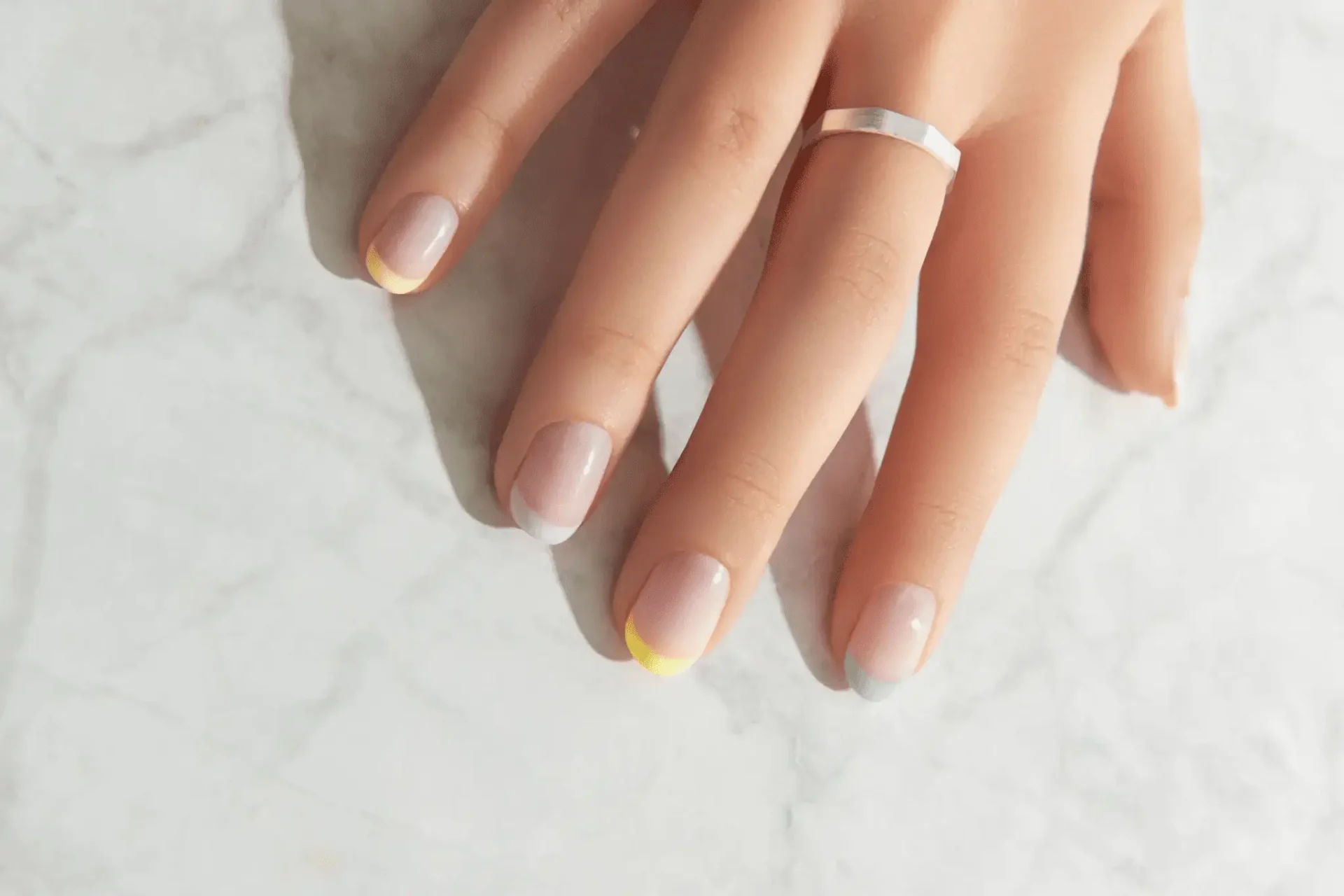 Hand with simple nail art, featuring a yellow accent on one nail.